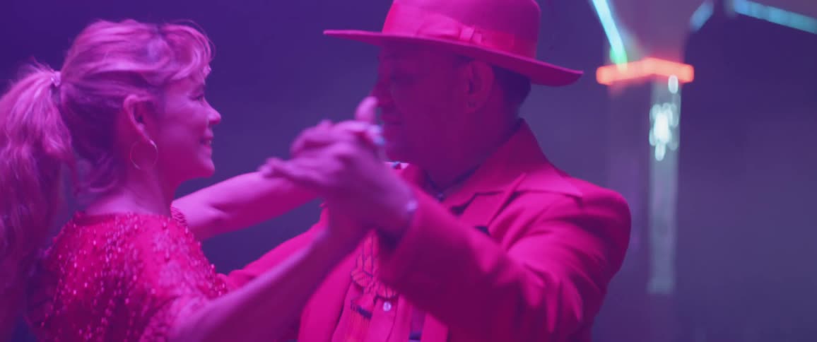 An older couple wearing 1940's costumes are dancing inside at night
