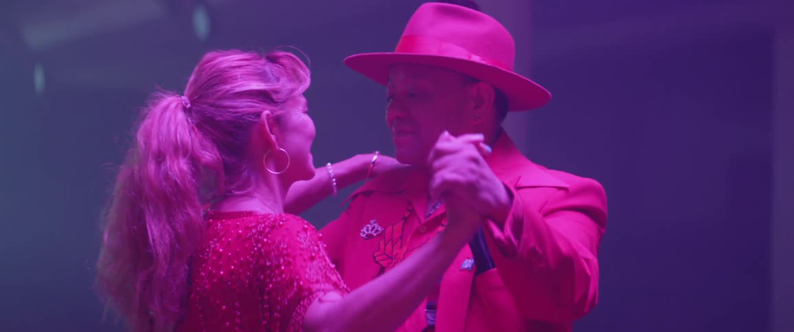 An older couple wearing 1940's costumes are dancing inside at night