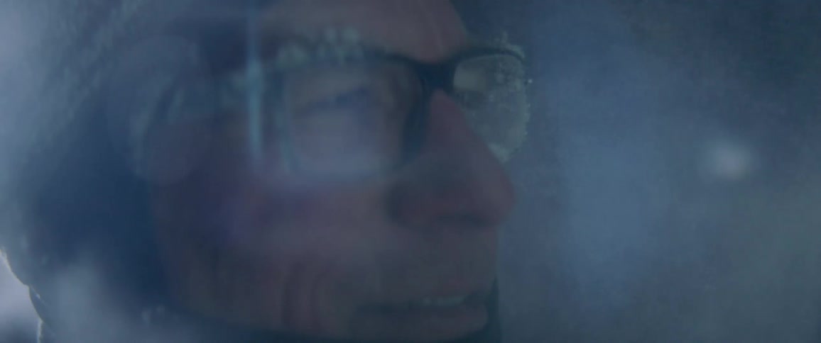 Man wearing glasses caked in ice smiles as smoke whirls around him