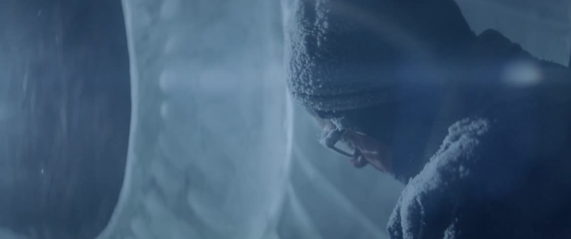 Man covered in frost looks down as beams of light shine on him