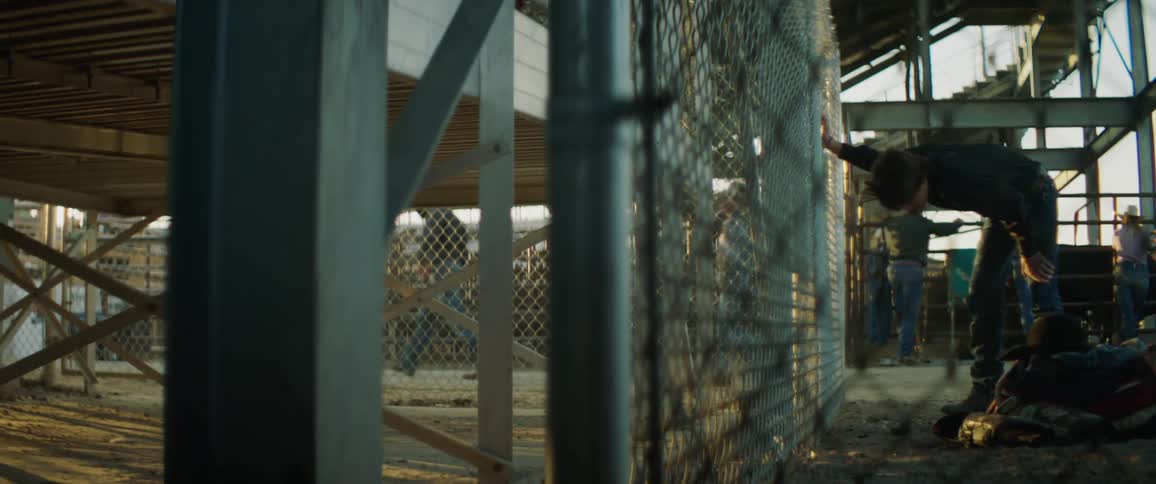 A person leans on a chain link fence while others walk past