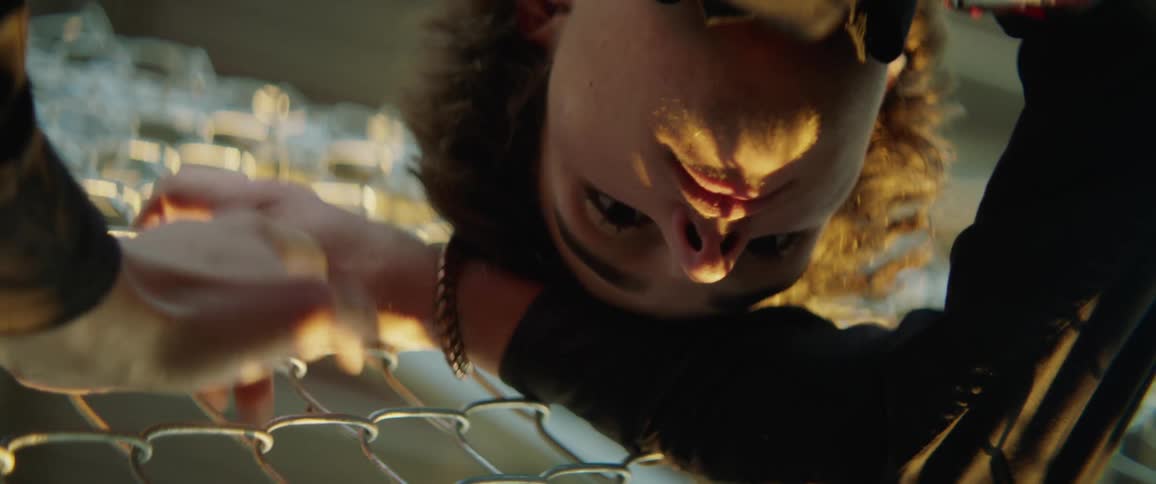 A man leans against a steel fence and wipes his mouth