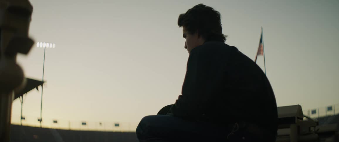 A man sits in a stadium at sunset