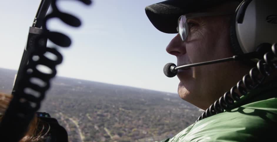 A pilot smiling and nodding at a passenger as he operates a helicopter