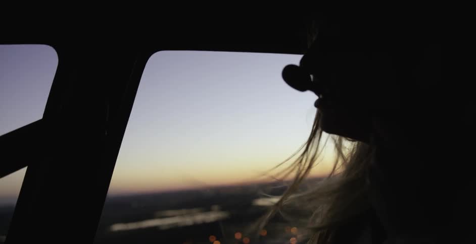 A woman's hair blows as she takes a helicopter ride over a city at dusk