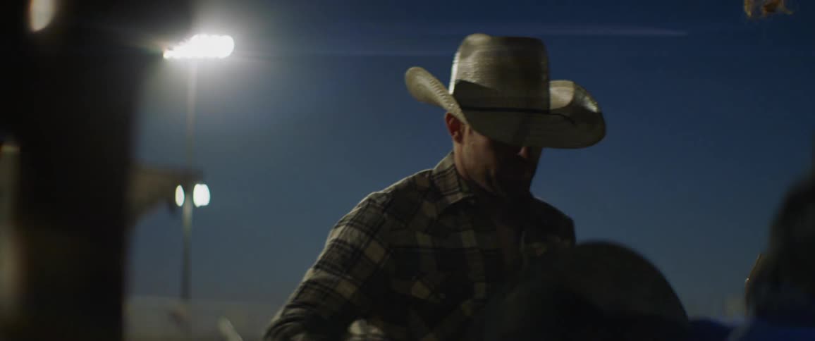 A cowboy is helping another cowboy at a rodeo as he prepares for his ride