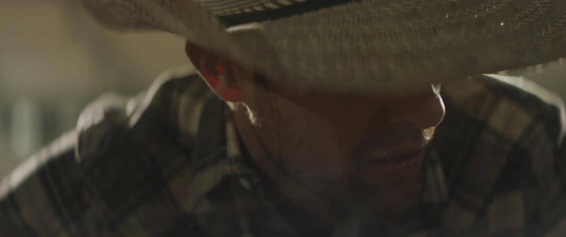 A man in a cowboy hat shifts under a light