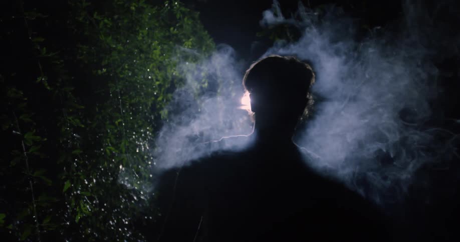 A man is walking outside at night with smoke coming from his face