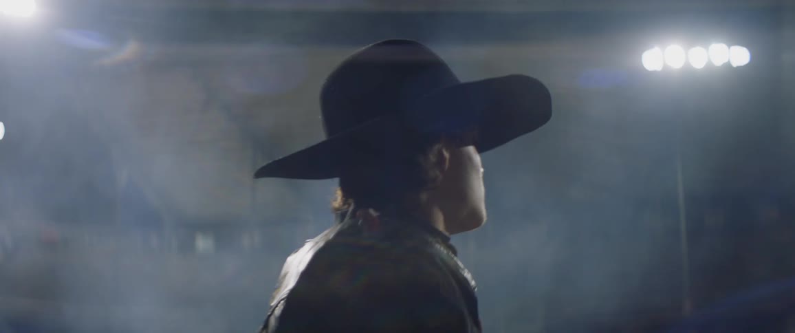 A cowboy walks in a dusty rodeo arena at night