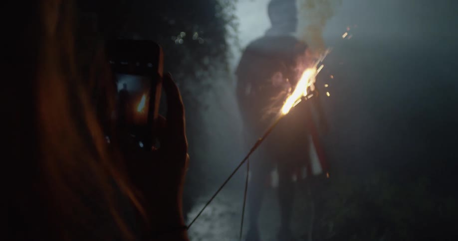 People are outside at night using sparklers and creating smoke