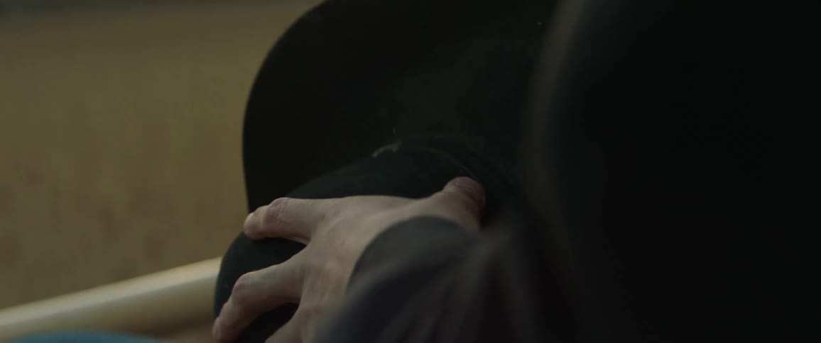 A man is rubbing his fingers over his hat as he stands outside