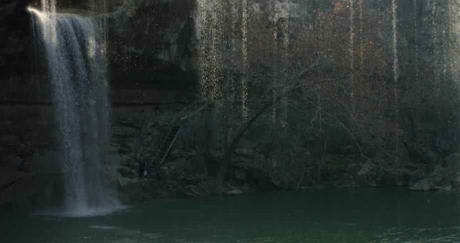 A waterfall is pouring into a stream in a dark area