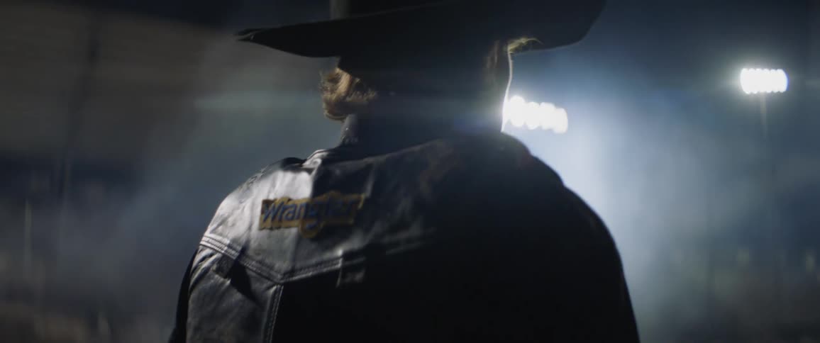 A man in a cowboy hate is walking in the fog at night