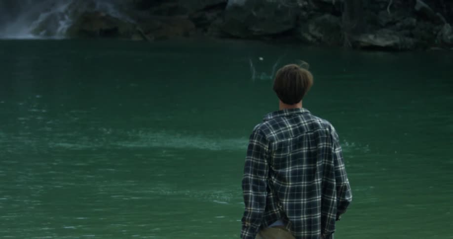 A man is standing by a lake then skips a rock over the water