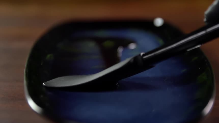 Chef wearing black latex gloves spreads sauce over a blue ceramic plate with a spatula