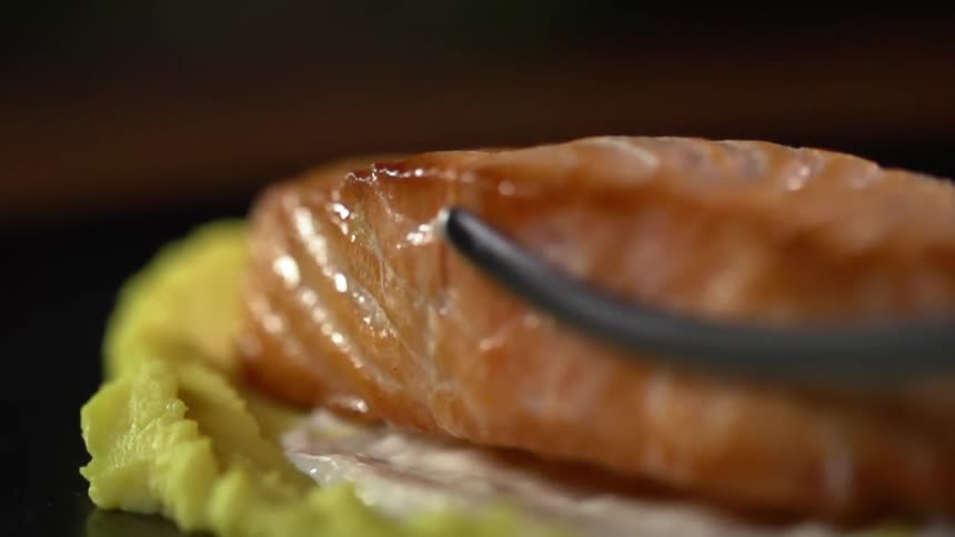 Tongs place a salmon fillet on a bed of sauce