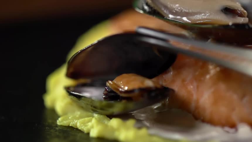 A metal utensil sets a clam down on a meal