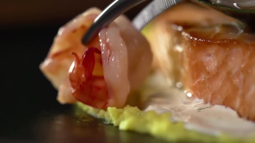 Metal tongs place a piece of meat next to a salmon fillet