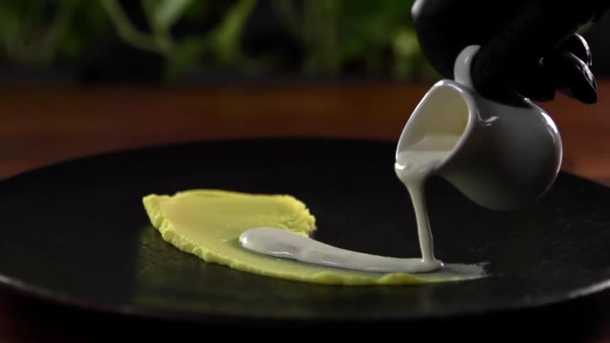 Chef with black latex gloves serves sauce with a white small jar on a black dish