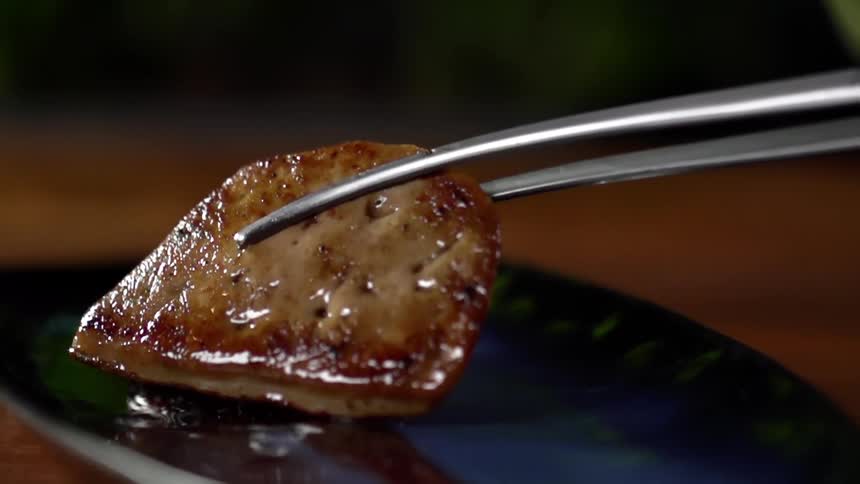 Slice of cooked meat served with pliers over a ceramic dish