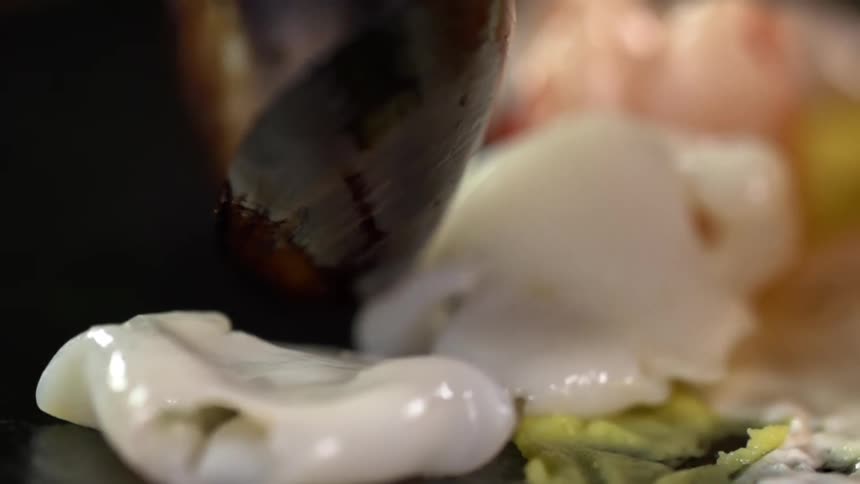 Cooked mussel being placed over other seafood in a plate