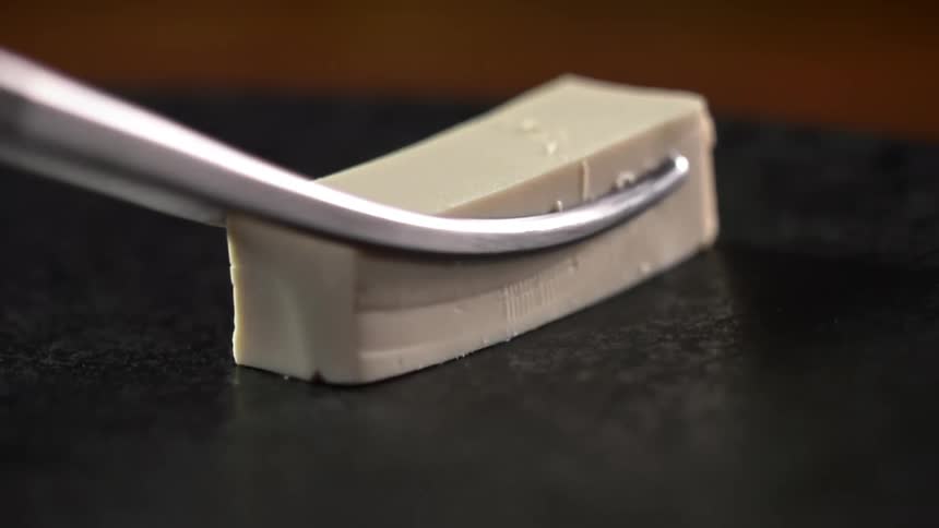 Metal tongs sit a bar of food on a black surface