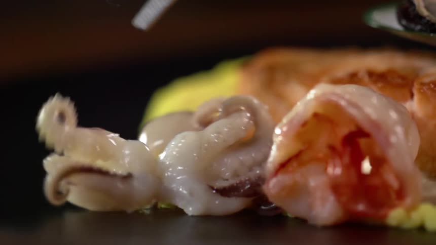 Cooked calamari plated in a black ceramic dish near yellow cream