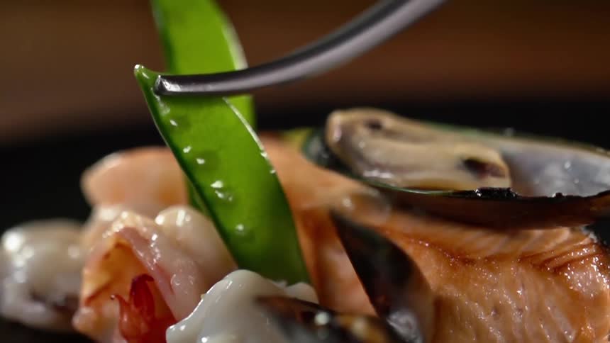 A person puts a pea pod on a seafood dish