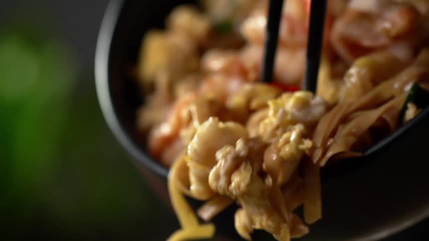 A person knocking noodles out of a bowl with chopsticks