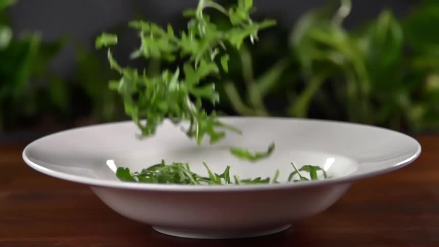 Arugula falling into a white serving bowl in slow motion