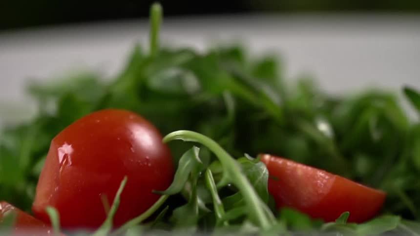 Tomatoes drop into a white bowl filled with greens