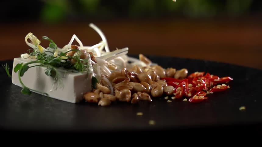 Red peppers fall on a plate spilling seeds next to an asian cuisine dish