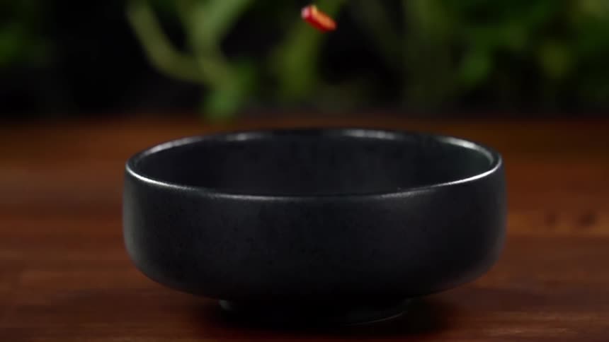 Finely chopped vegetables fall inside a black ceramic bowl on a wooden table