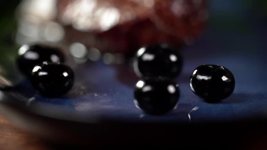 Several black olives drop and bounce on a plate
