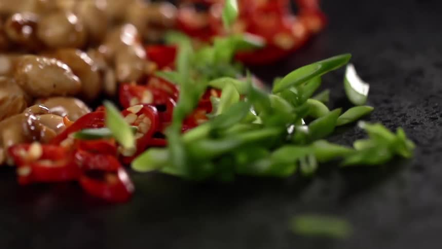 Garnish is sprinkled onto a plate next to chopped red peppers