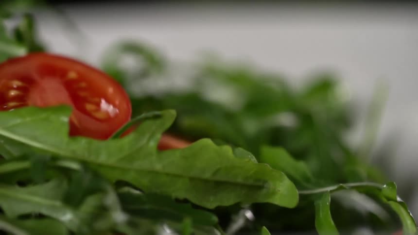 Tomato slices drop onto bed of salad greens on flat pale surface