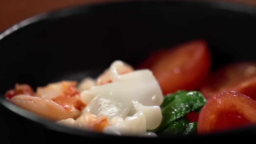 A white food substance drops into a pan filled with vegetables