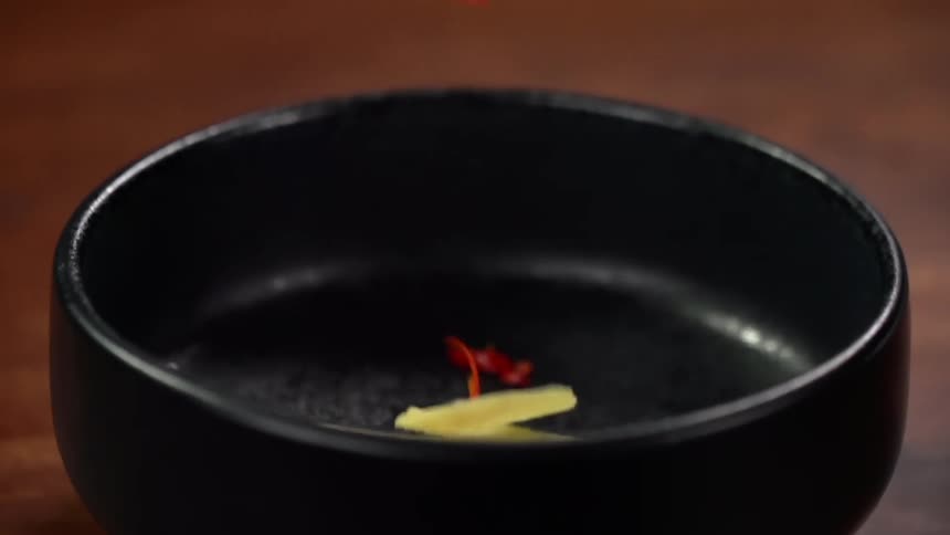 A few vegetable pieces drop into a black bowl