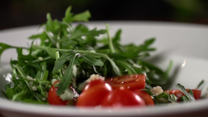 Sliced tomatoes fall over leafy green salad inside a white ceramic bowl
