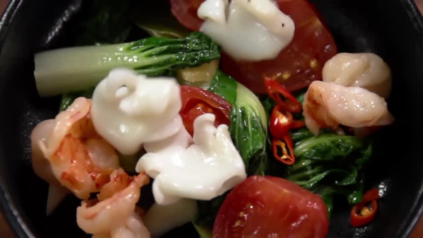 Food is added to a frying pan with vegetables in it