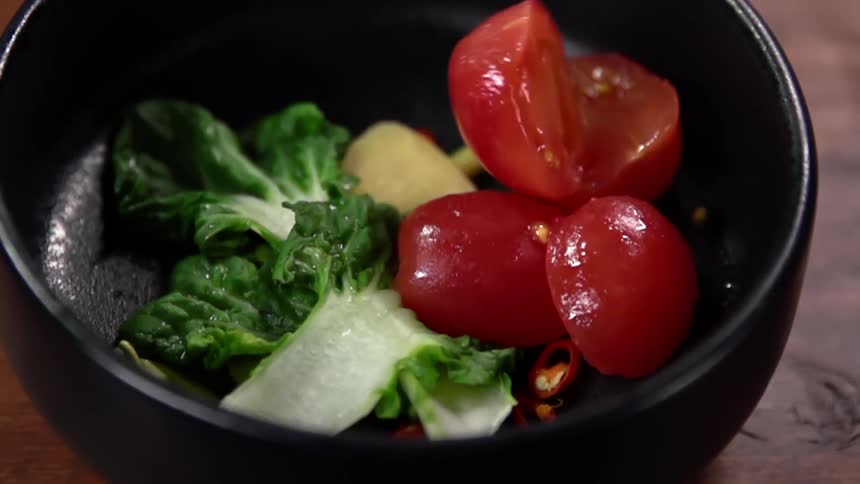 Sliced tomatoes and leafy greens inside a black ceramic bowl