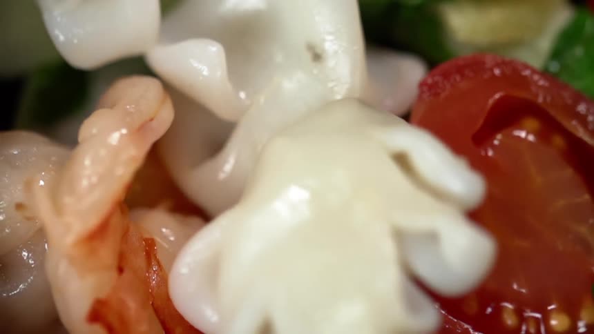 Chunks of white mushrooms are added to a dish containing shrimp and other vegetables
