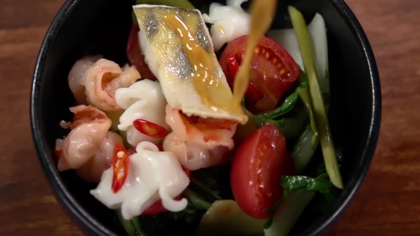 Sauce being poured into a bowl of vegetables that is on a table