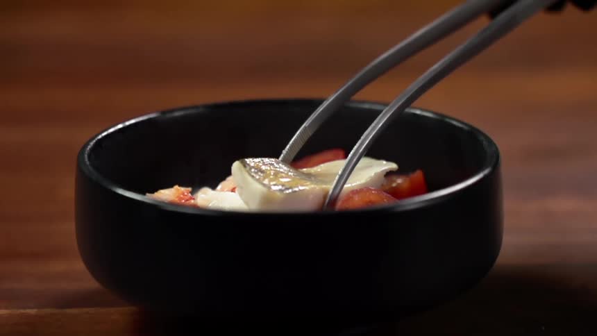 Metal tongs set a piece of food in a bowl