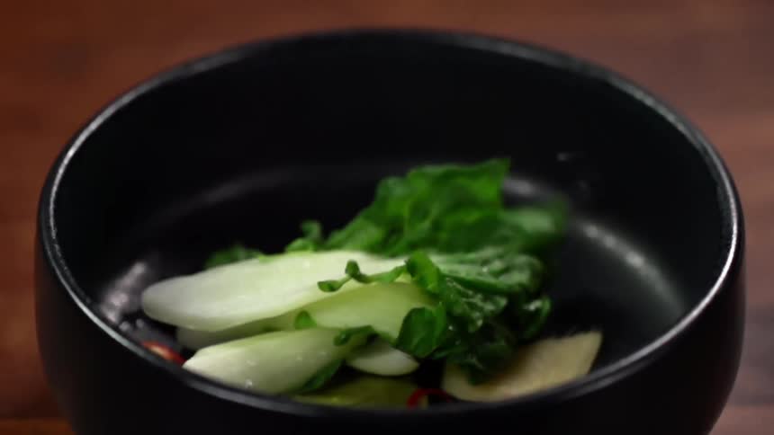 Vegetables falling into a black ceramic bowl over a wooden table