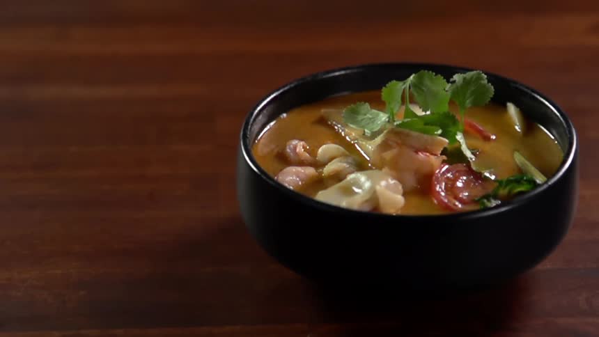 Fresh herb leaves fall into a ceramic bowl with soup over a wooden table