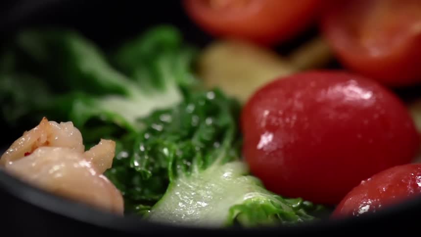 Shrimp dropping on a bed of leafy greens and tomatoes in slow motion