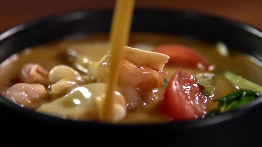 Liquid pours onto meal in black container full of vegetables and meats shining in light