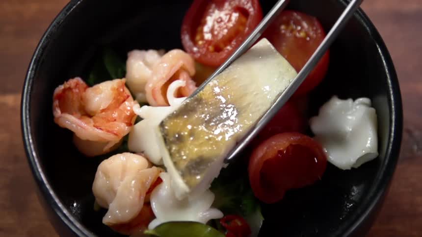 Using chopsticks to place fish meat on a black ceramic bowl with asian food