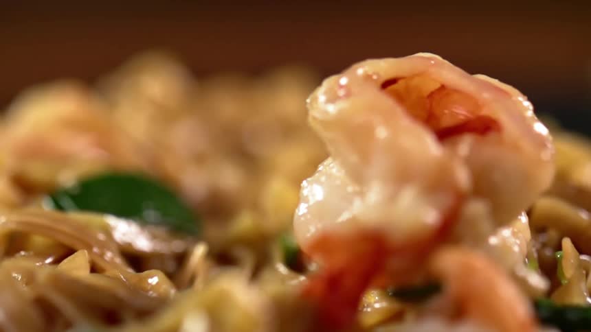Cooked shrimp are dropped onto a plate of chow mein noodles